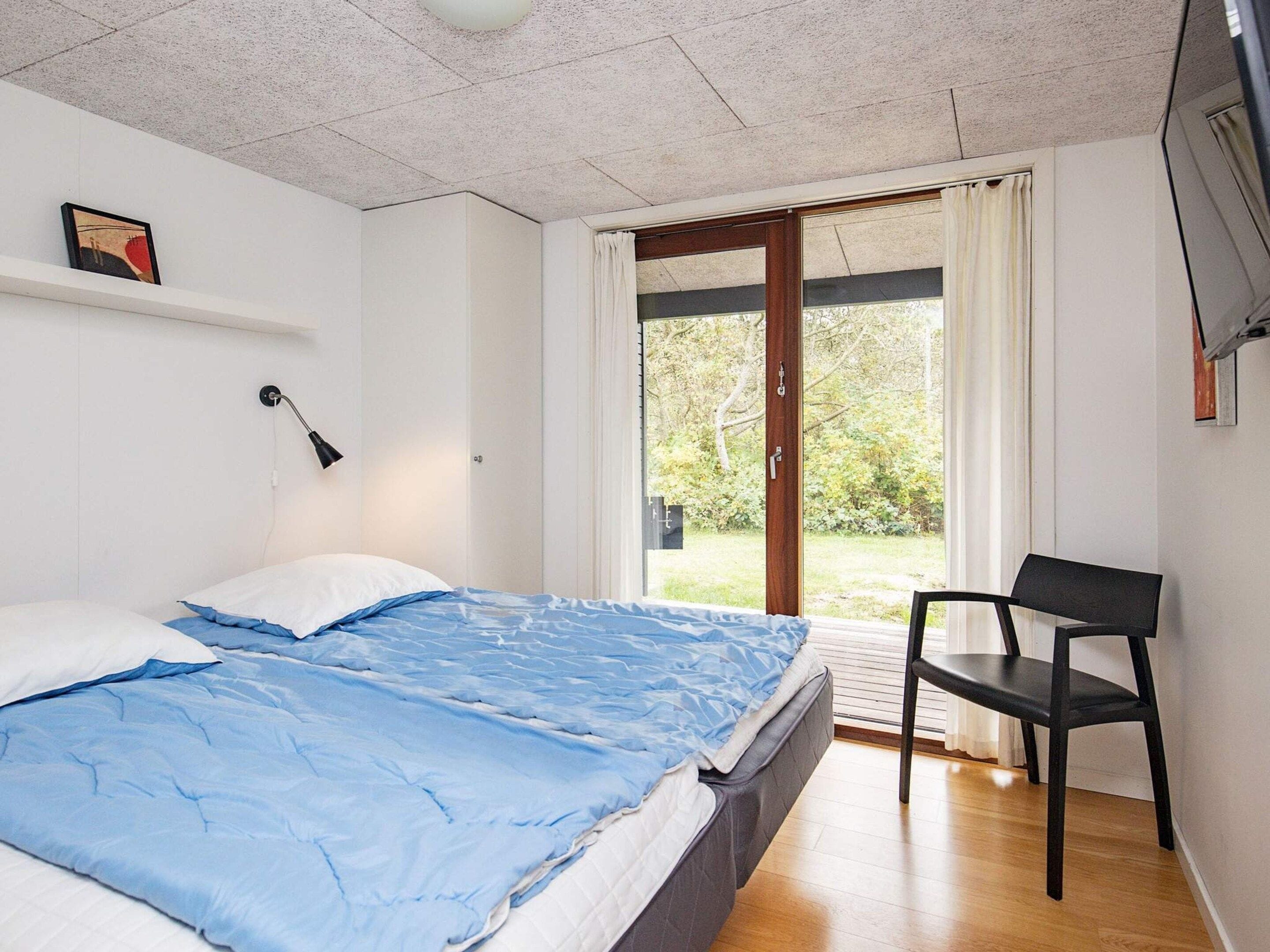 A bedroom with a bed, a chair, a window, and a door leading to a balcony.
