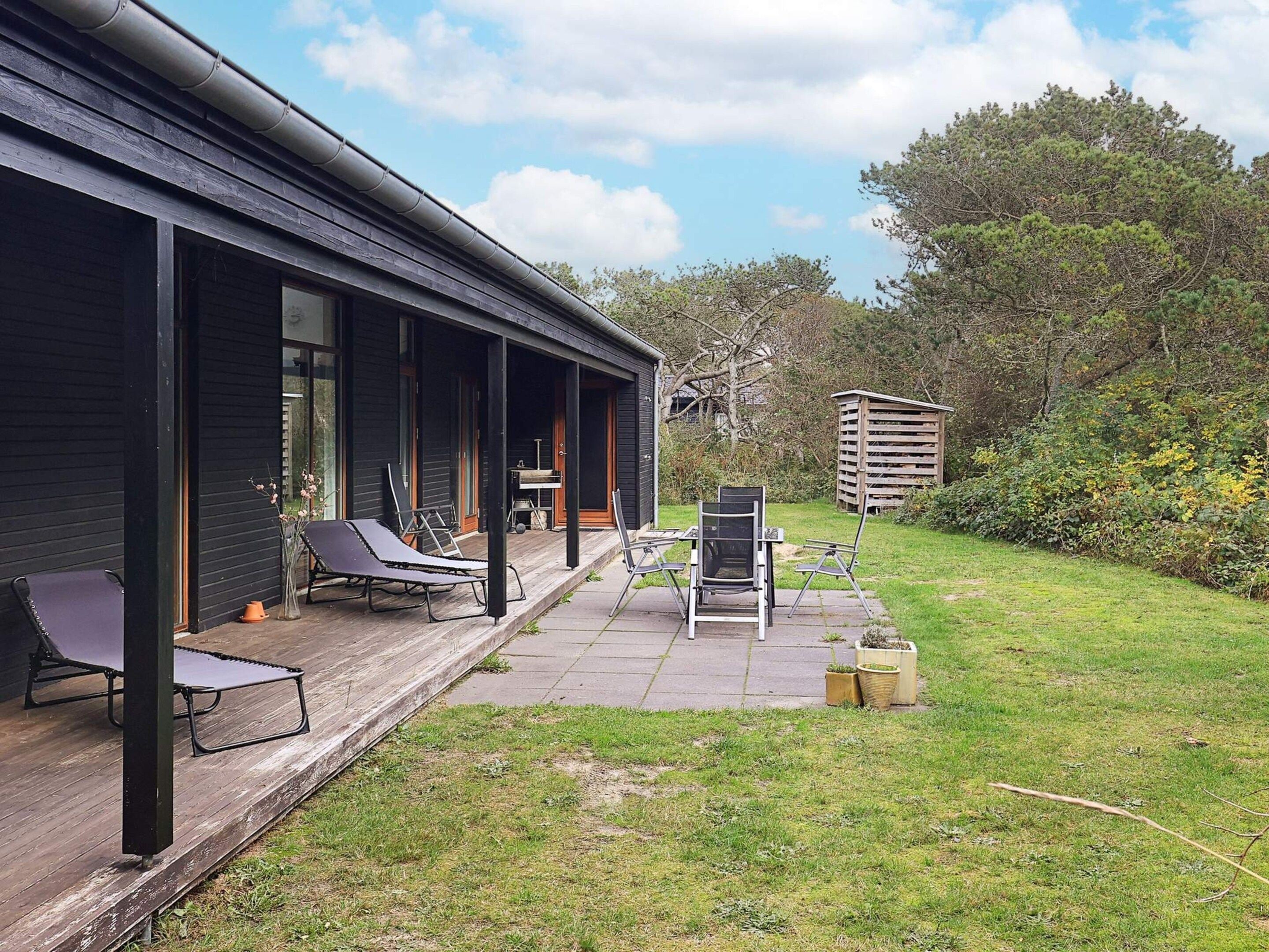 A modern building with a covered patio area featuring lounge chairs and a table.