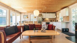 Una cocina moderna con armarios de madera, una zona de comedor con mesa de madera y sofá de cuero, y ventanas amplias que aportan luz natural.
