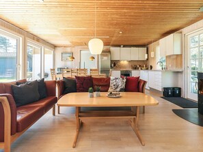 A modern kitchen with wooden cabinets, a dining area with a wooden table and leather sofa, and large windows providing natural light. - 8 Person Holiday Home in Lokken (Lokken)