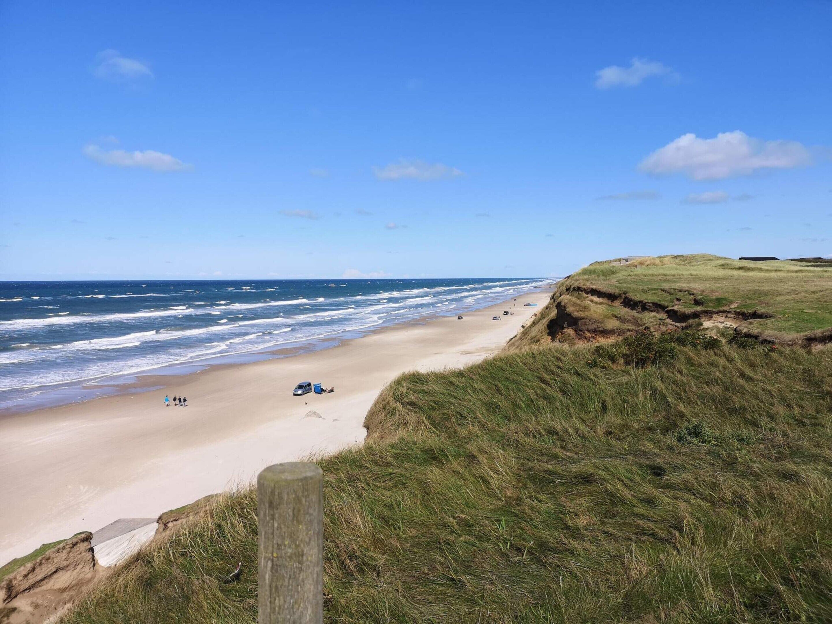 A beach with a grassy cliff, a sandy shore, and the ocean.