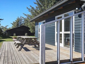 A wooden deck with a picnic table, a covered area, and a building with large windows.