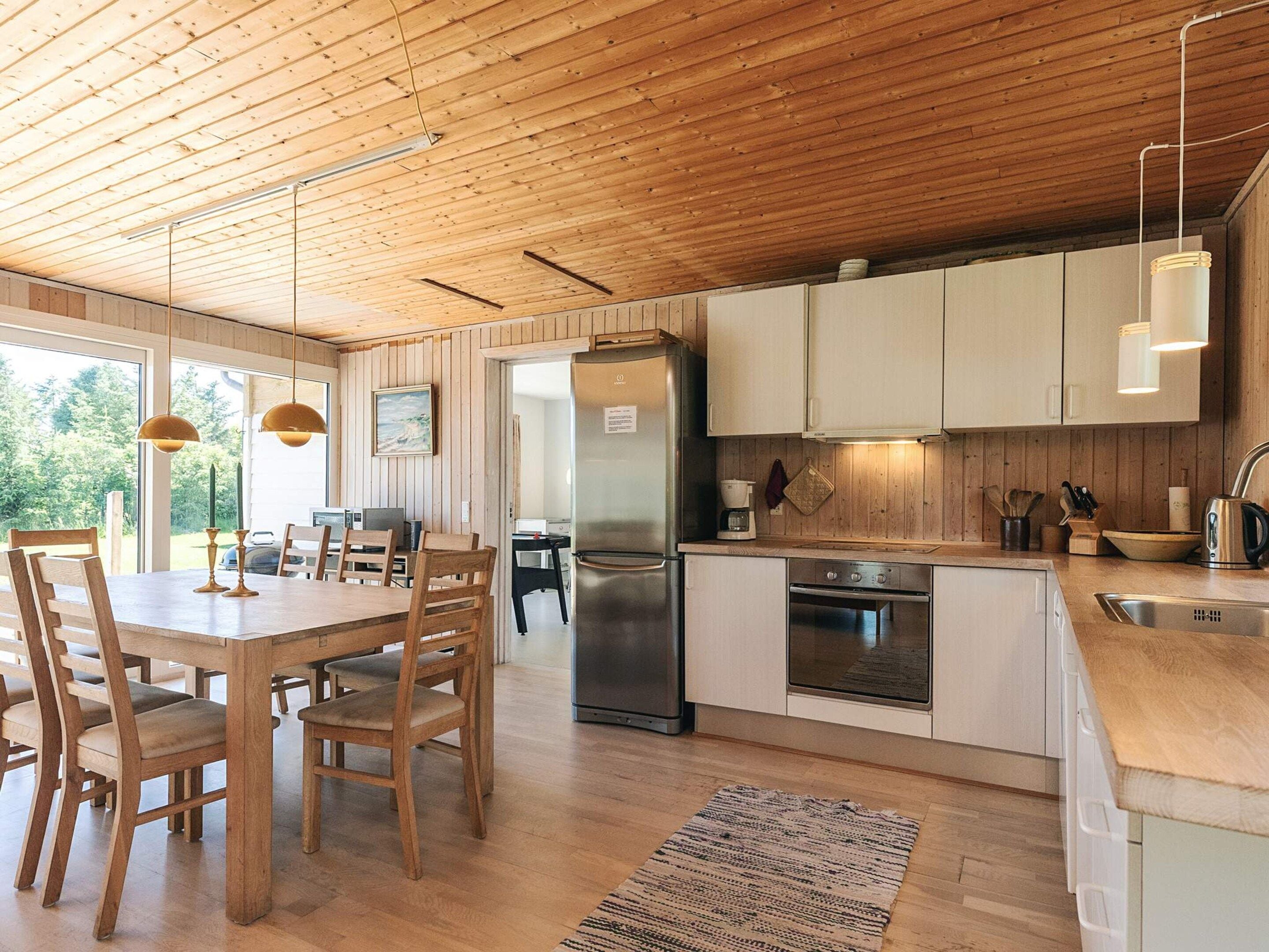 A modern kitchen with wooden cabinets, a stainless steel refrigerator, and a dining area with wooden chairs and a table.