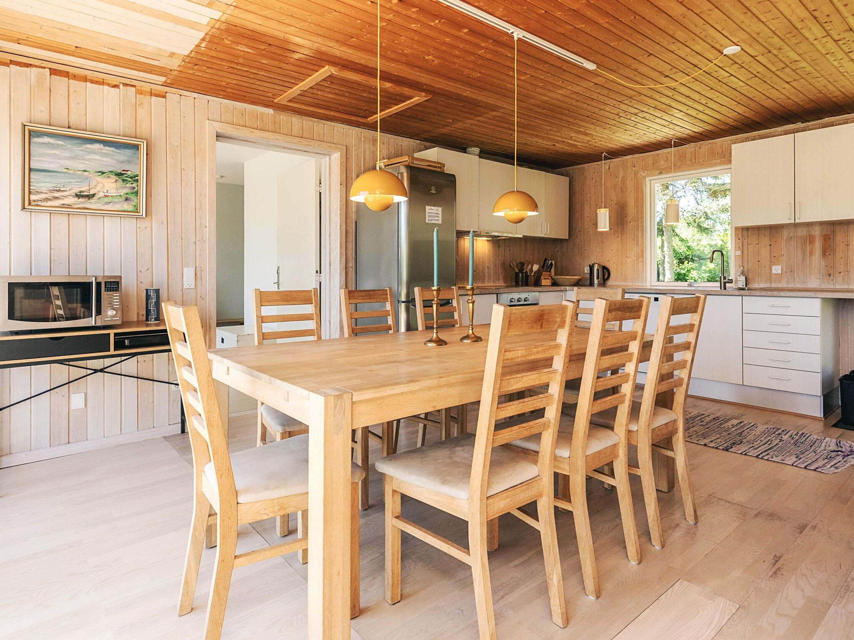 A wooden dining table with six chairs, a kitchen with white cabinets, and a wooden ceiling.
