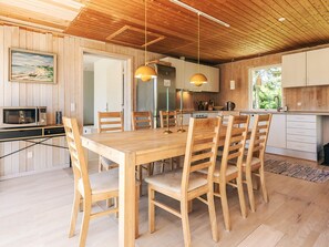 A wooden dining table with six chairs, a kitchen with white cabinets, and a wooden ceiling. - 8 Person Holiday Home in Lokken (Lokken)