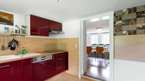Une cuisine moderne avec des meubles rouges, un four encastré et un coin repas avec des chaises en bois.