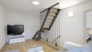 A modern living room with a flat-screen TV, a white entertainment unit, a glass coffee table, a grey sofa, a wooden staircase, and a white wall with a textured pattern. - Modern Holiday Home With Jacuzzi (Medulin)