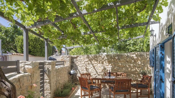 A patio with a stone wall, wooden furniture, and a pergola with grapevines. - Modern Holiday Home With Jacuzzi (Medulin)