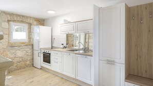 A modern kitchen with white cabinets, a stone accent wall, and a wooden countertop. - Modern Holiday Home With Jacuzzi (Medulin)