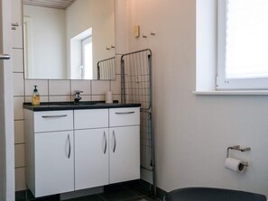 A bathroom with white cabinets, a black countertop, a mirror, a towel rack, and a toilet paper holder.