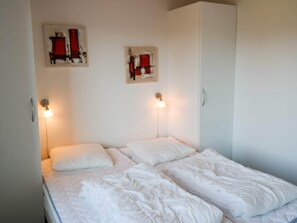 A single bed with white bedding in a room with white walls and two wall-mounted light fixtures.