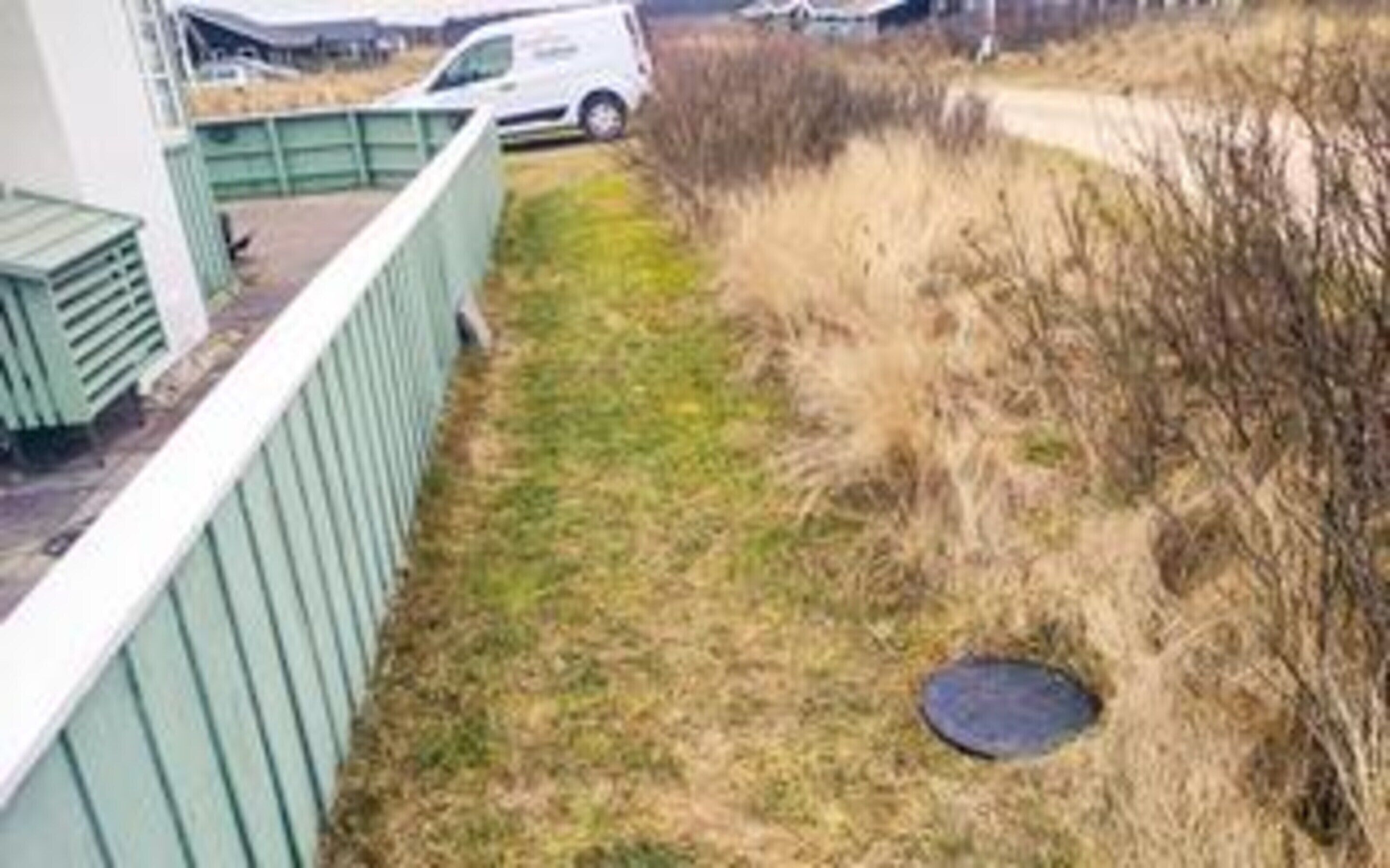 Een grasveld met een afvoerrooster en een pad dat naar een gebouw leidt.