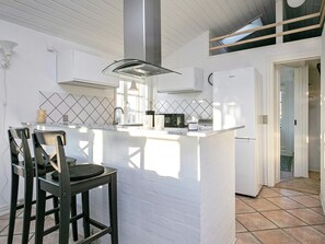 A modern kitchen with white cabinetry, a central island, and a dining area with two chairs. - Holiday Home in LÃ¸kken (Lokken)