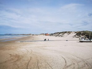 A sandy beach with footprints, a boat, and a dune in the background.