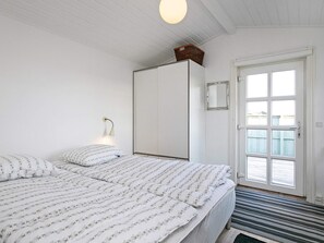A bedroom with a bed, a bedside lamp, a wardrobe, a door with a view, and a window.