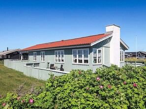 A two-story building with a red roof, large windows, and a balcony with outdoor furniture. - Holiday Home in LÃ¸kken (Lokken)