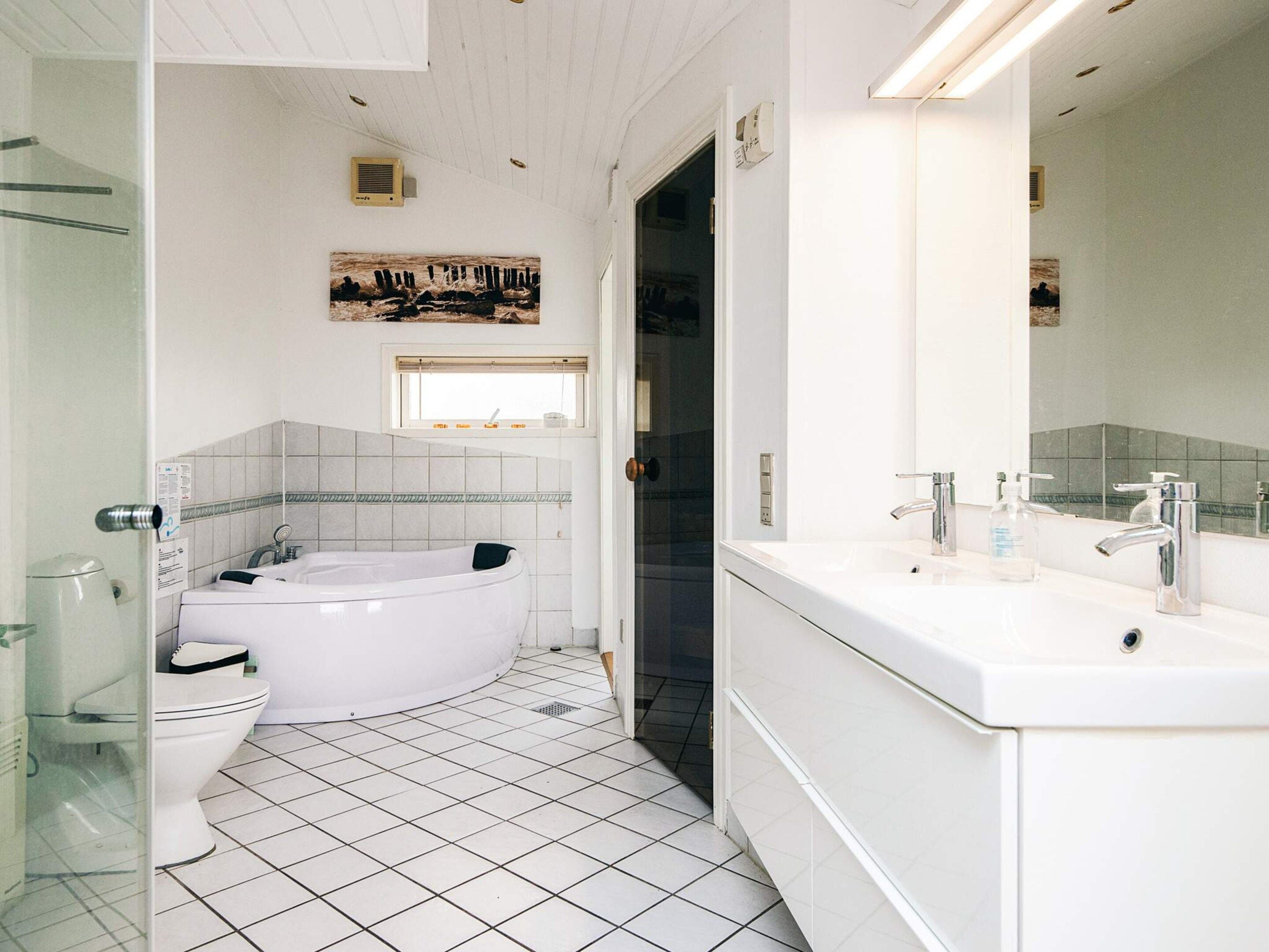 Ein Badezimmer mit einer weißen Badewanne, einer Toilette und einem Waschbecken mit Spiegel.
