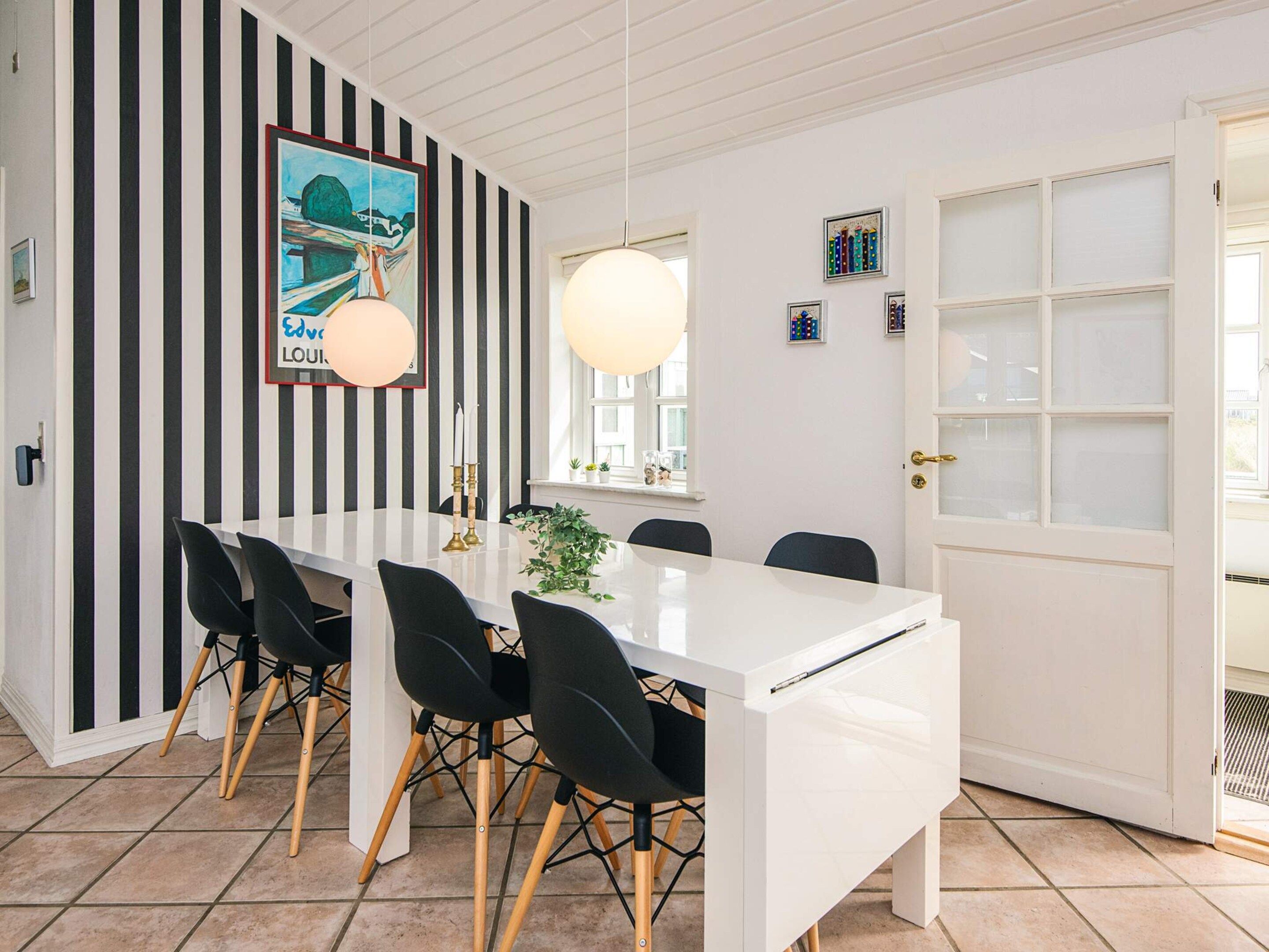 A dining area with a white table, black chairs, and a striped wall.