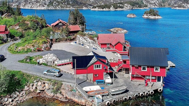 A coastal property with red buildings, a dock with boats, and a clear view of the sea and rocky hills in the background. - 6 Person Holiday Home in Brandasund (Bomlo)