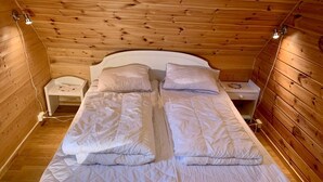A wooden cabin bedroom with two beds, each with white bedding and a quilted duvet. There are bedside tables with lamps and a small nightstand. - 6 Person Holiday Home in Brandasund (Bomlo)
