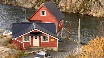 A red building with a black roof, a small porch, and a car parked in front.
