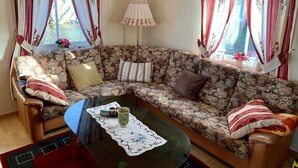 A cozy living room with a floral-patterned sofa, a glass coffee table, and curtains with floral designs. - 6 Person Holiday Home in Brandasund (Bomlo)