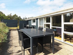 En udendørs terrasse med bord og stole, en lille siddeplads og udsigt til en bygning med store vinduer.