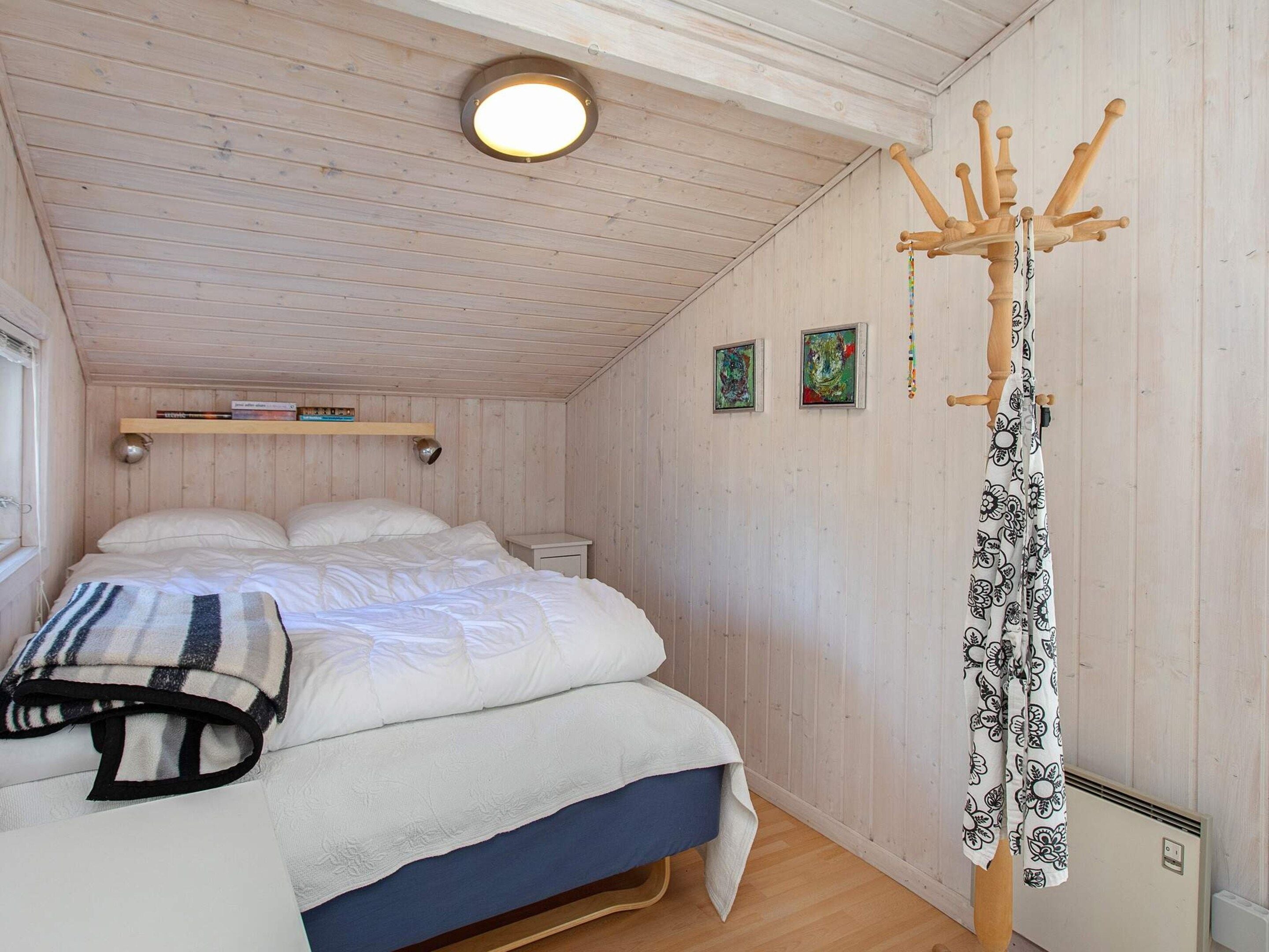 A bedroom with a bed, a bedside table, a hanging coat rack, and two framed pictures on the wall.