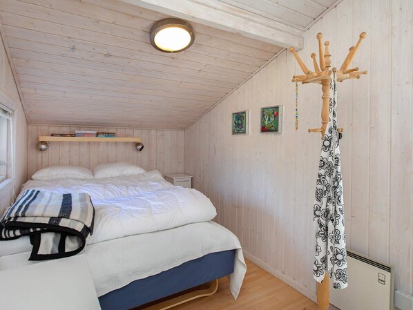 A bedroom with a bed, a bedside table, a hanging coat rack, and two framed pictures on the wall.