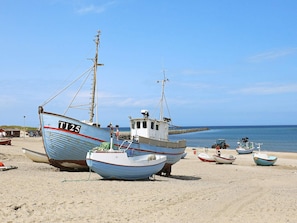 Una playa con varios barcos, incluyendo uno grande marcado T125, y un tractor sobre la arena.