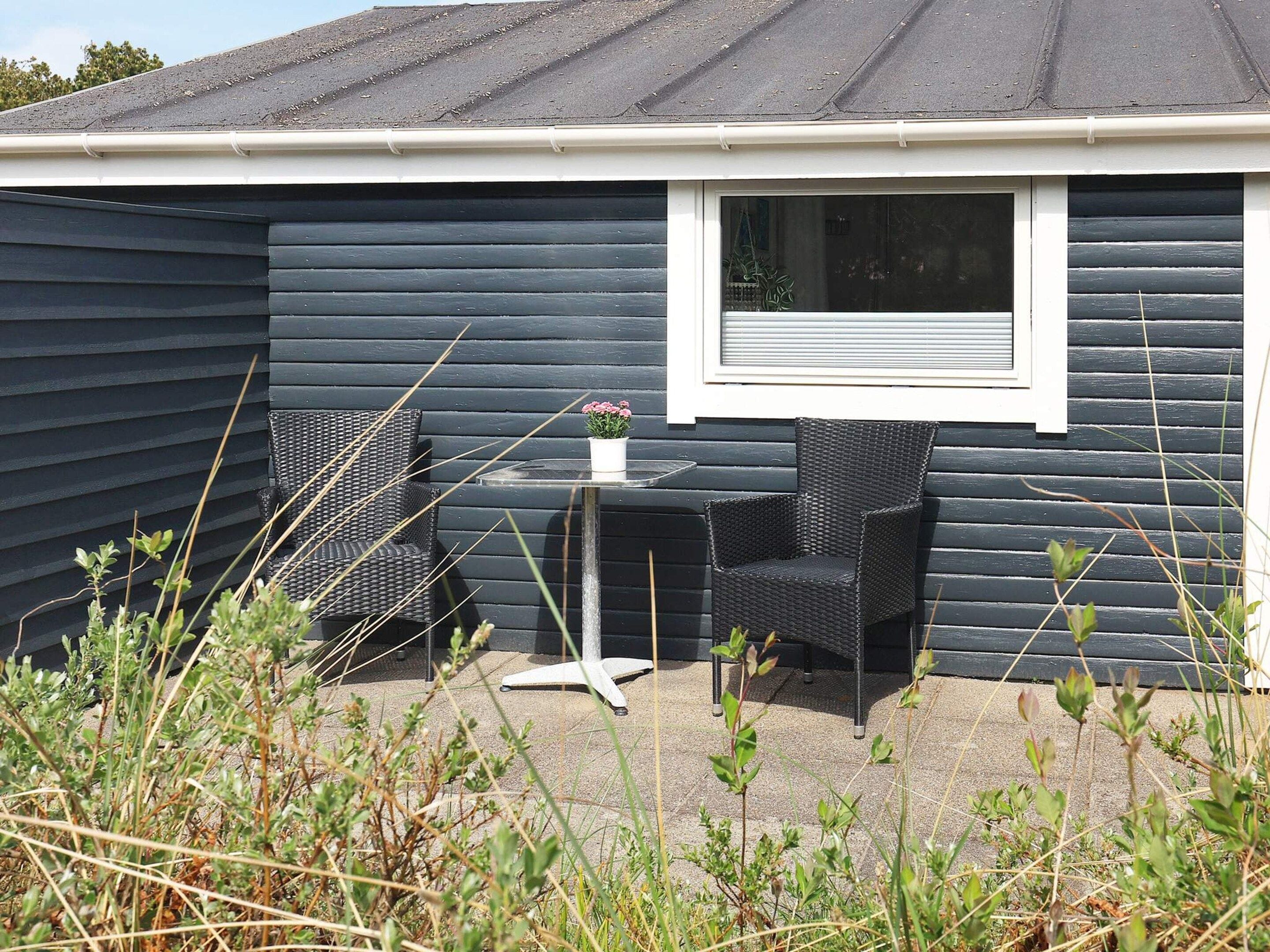 A dark-colored building with a window, two wicker chairs, a small table, and a potted plant.