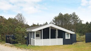 A small, single-story cabin with a porch, surrounded by trees and a gravel path. - 4 Person Holiday Home in Thisted (Thisted)