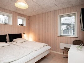 A bedroom with a bed, a desk, and a window with blinds.