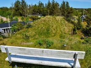 A wooden bench overlooking a grassy hill with houses in the background.