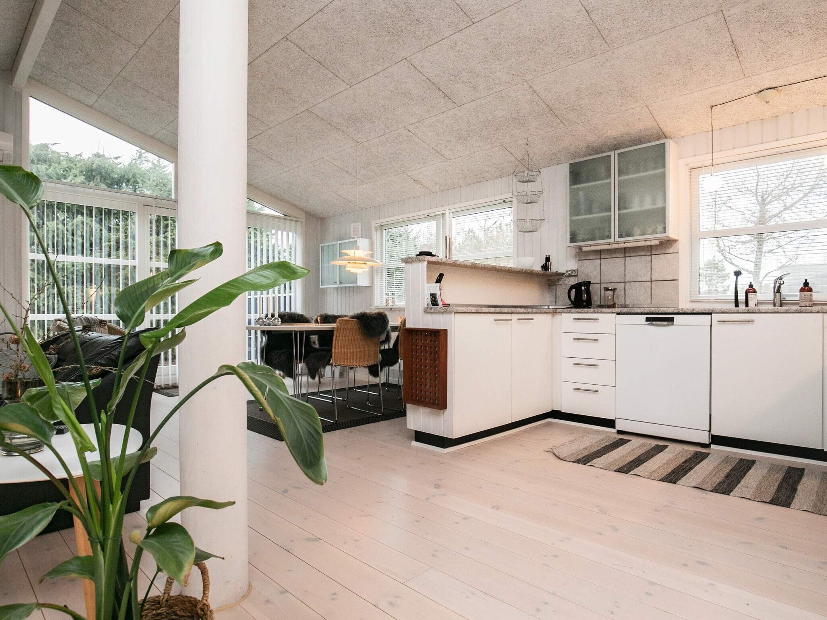 Eine moderne Küche mit weißen Schränken, ein Essbereich mit Tisch und Stühlen sowie große Fenster, die für natürliches Licht sorgen.