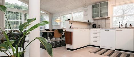 Eine moderne Küche mit weißen Schränken, ein Essbereich mit Tisch und Stühlen sowie große Fenster, die für natürliches Licht sorgen.