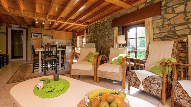 A cozy living room with a stone wall, wooden ceiling beams, and a dining area with a table and chairs. - Renovated Farmhouse From 1832 With Beautiful View of Winter Sports Area (Vielsalm)