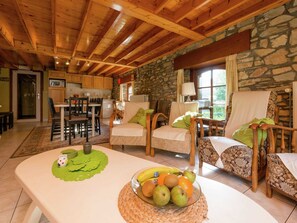 A cozy living room with a stone wall, wooden ceiling beams, and a dining area with a table and chairs. - Renovated Farmhouse From 1832 With Beautiful View of Winter Sports Area (Vielsalm)