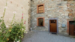 A stone building with a gravel courtyard, a wooden door, and a window with a shutter. - Renovated Farmhouse From 1832 With Beautiful View of Winter Sports Area (Vielsalm)