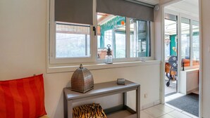 Ein modernes Wohnzimmer mit einer Couch, einem Konsolentisch mit Dekoration und Blick durch ein Fenster mit einer Jalousie.