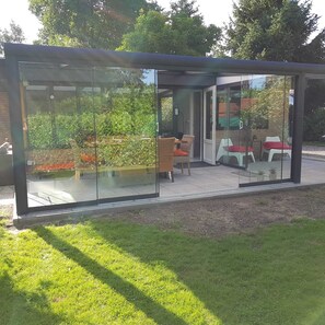 Une véranda moderne en verre, dotée d’un espace patio, de sièges extérieurs et offrant une vue sur le jardin.