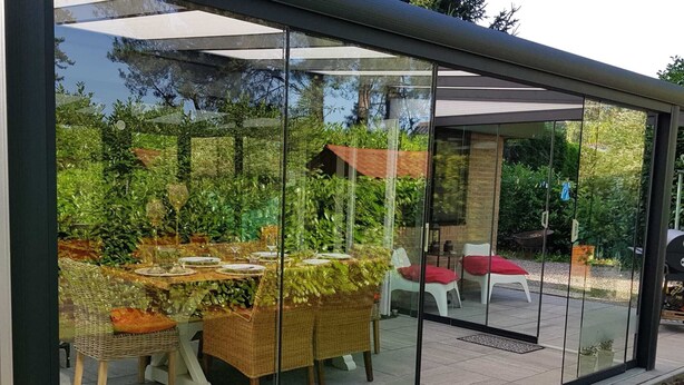 Ein moderner Essbereich im Freien mit Korbmöbeln und Glaswänden.