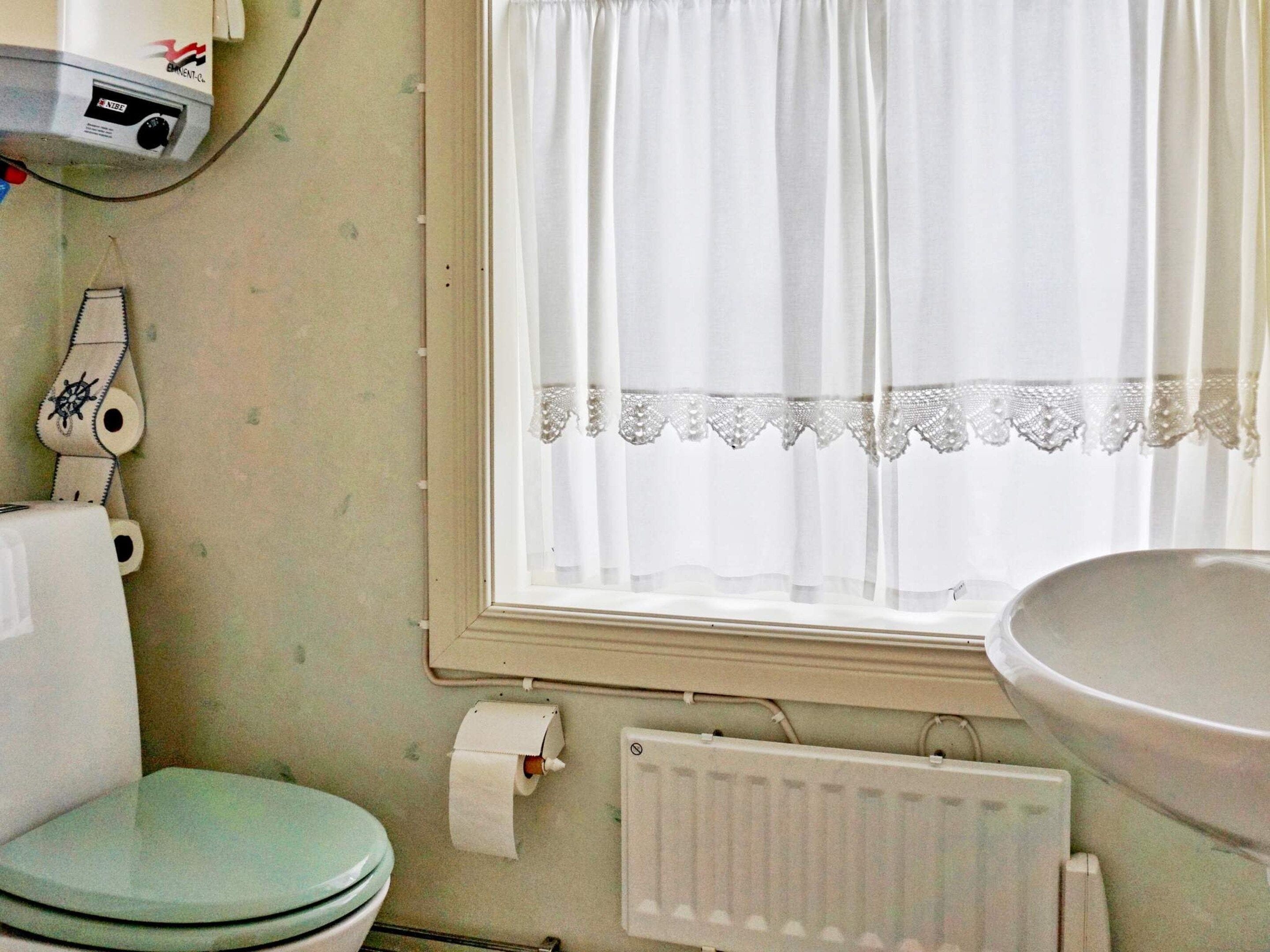 Ein Badezimmer mit Toilette, Heizkörper, einem Fenster mit Vorhängen und einem Waschbecken.