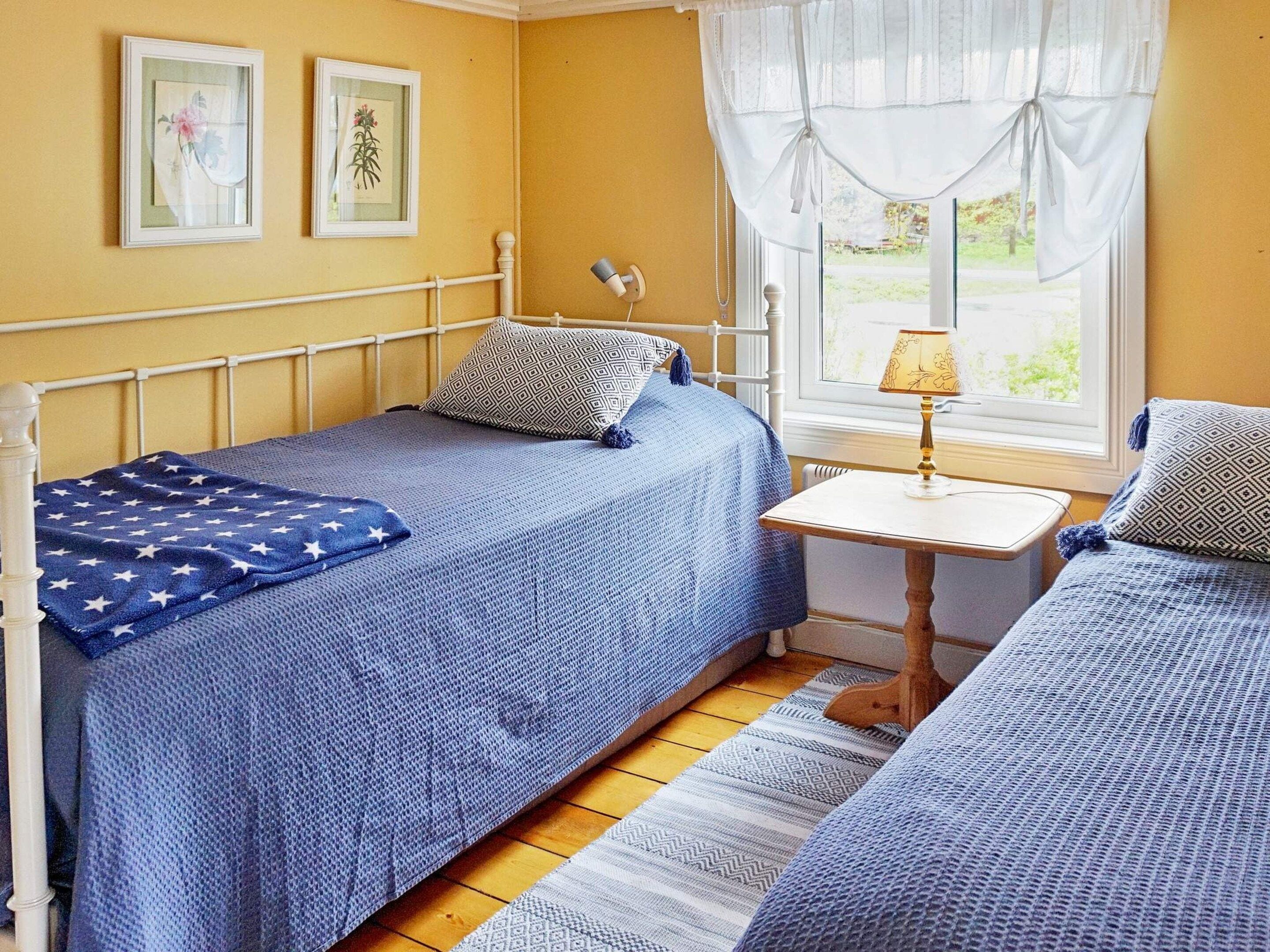 A bedroom with two beds, a bedside table, a lamp, and a window with curtains.