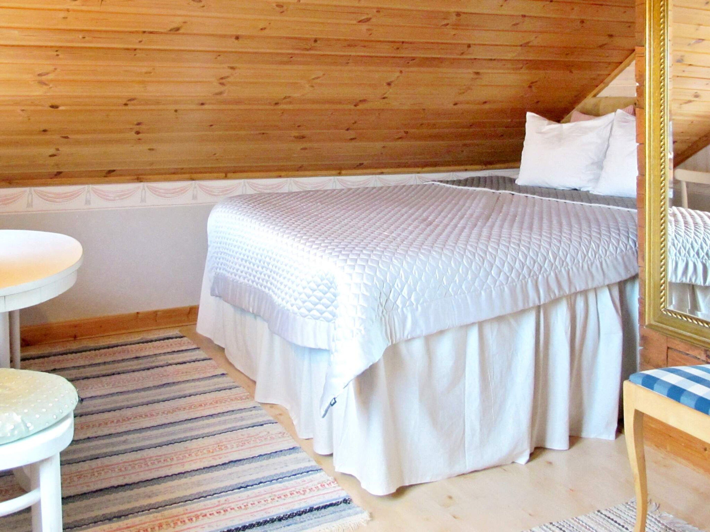 Un dormitorio con cama, mesita de noche, una silla, un espejo y alfombra estampada.