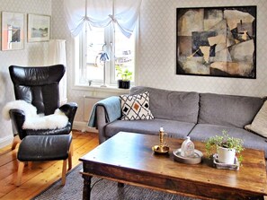 A living room with a leather armchair, grey sofa, wooden coffee table, and a painting on the wall. - 7 Person Holiday Home in Grisslehamn (Grisslehamn)