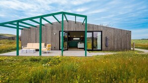Une maison moderne en bois, dotée d’un espace extérieur aménagé et couvert, et dont la cuisine est visible à travers des portes vitrées.