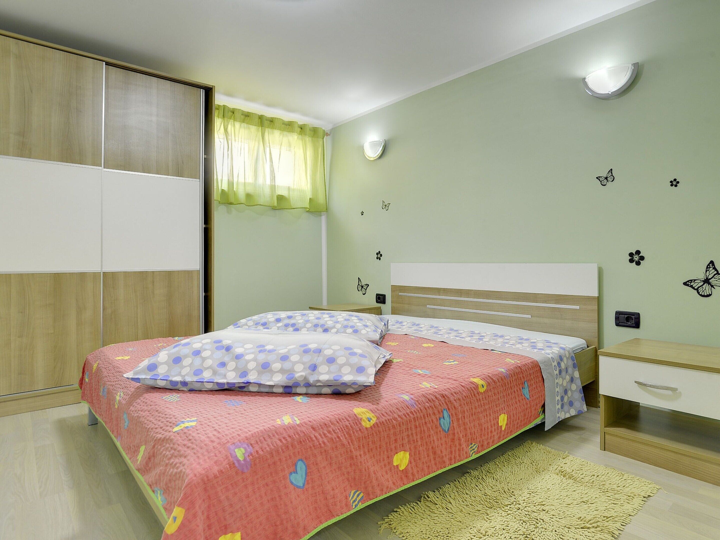 A bedroom with a bed, a nightstand, a wardrobe, and a window with curtains.