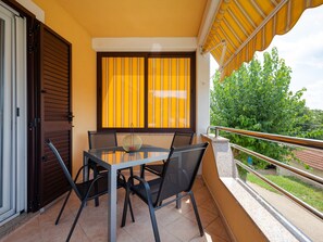 A balcony with a table and chairs, a window with yellow curtains, and a view of greenery. - Villa in Baksi With Pool and Playground (Pazin)
