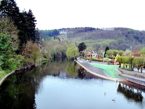 A river with a bridge, trees, and a building with a green roof.